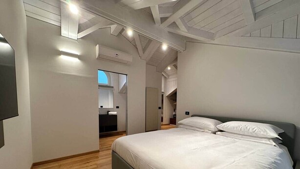 Un dormitorio con una cama grande, suelo de madera y un diseño moderno en el techo.