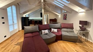 Un loft amplio con techo alto, vigas de madera y un gran sofá modular con cojines.