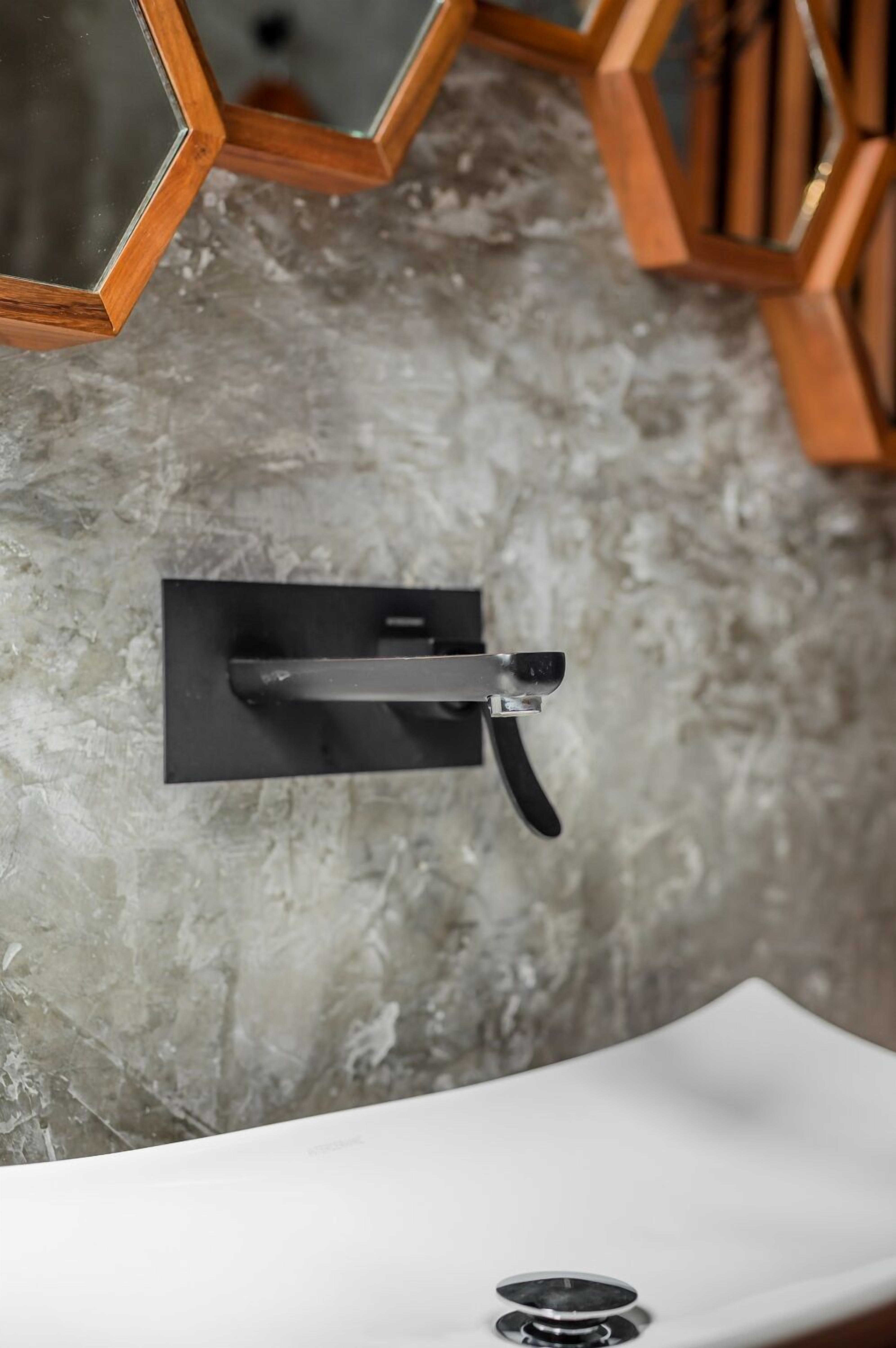 Un baño con un lavamanos blanco, un grifo negro y una pared gris con textura.