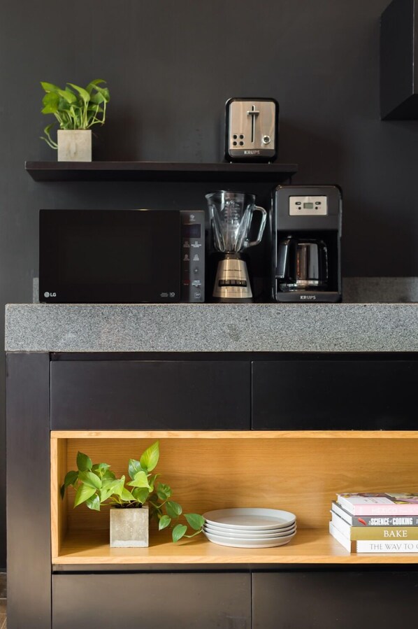 A modern kitchen with a built-in microwave, coffee maker, and toaster. There is a shelf with a plant and a stack of books.
