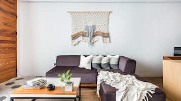 Una sala moderna con un sofá oscuro, una mesa de centro de madera y un colgador de macramé en la pared.