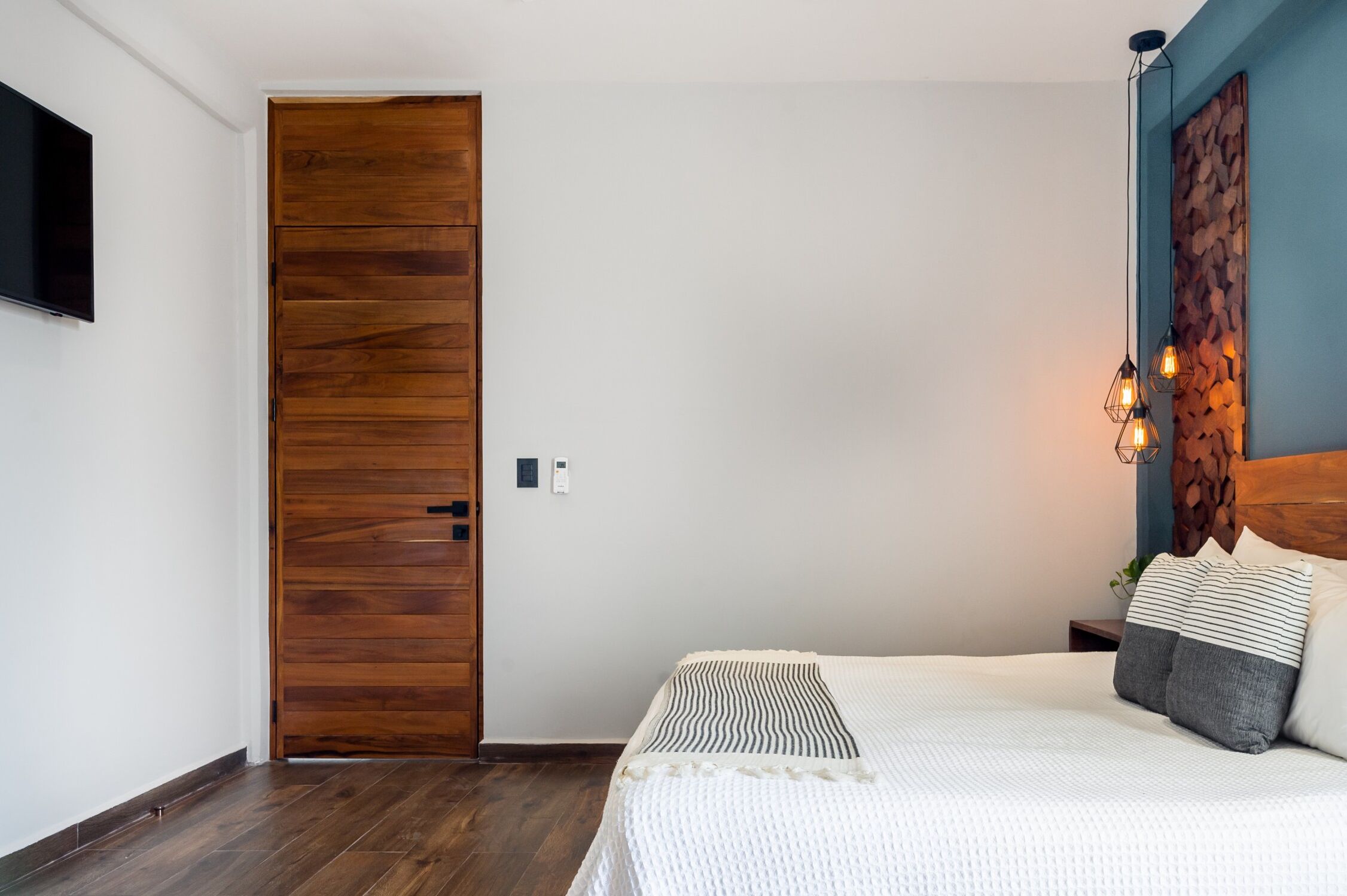 A bedroom with a wooden door, a bed with striped bedding, and a wall-mounted TV.