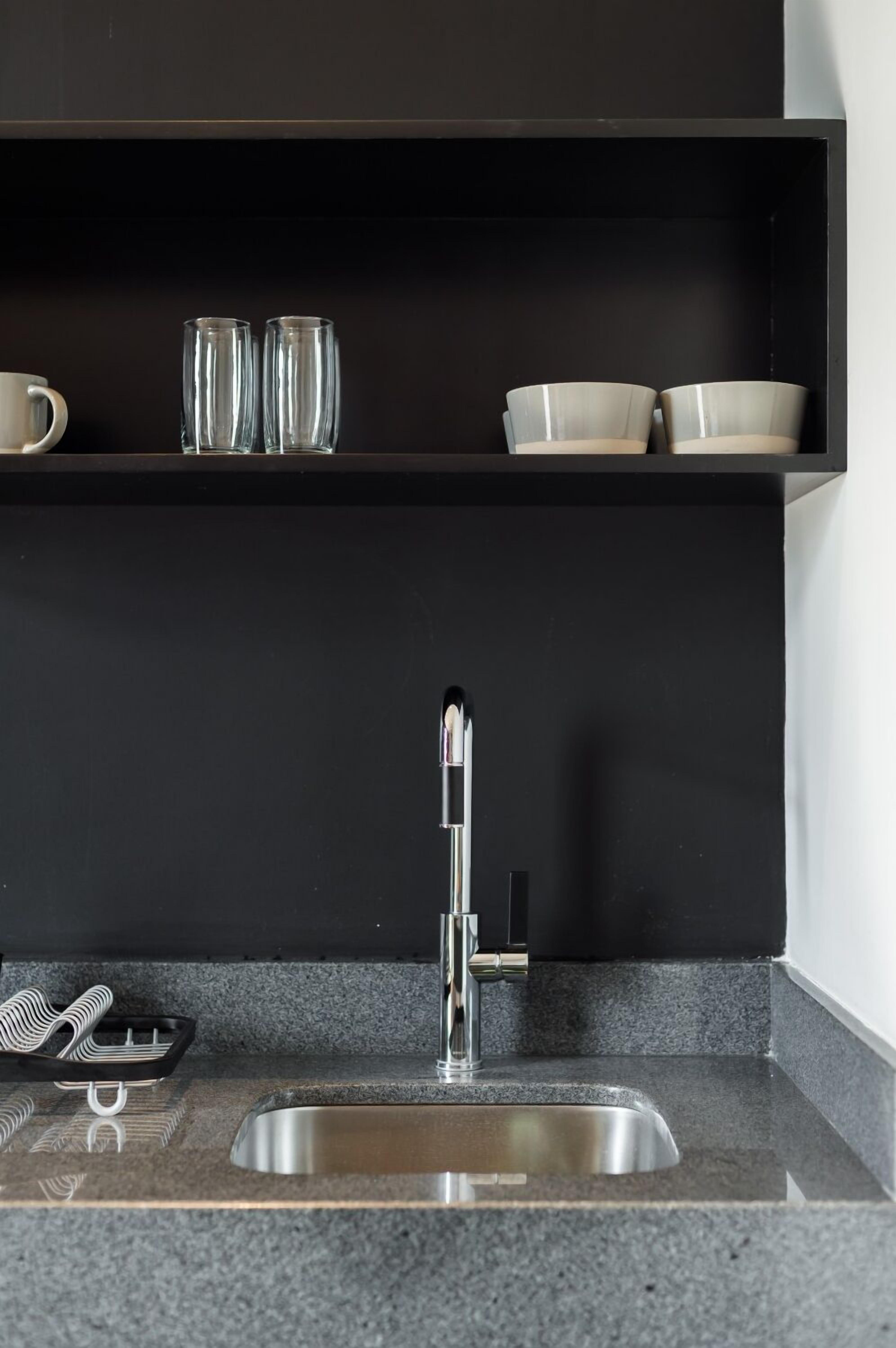 A modern kitchen with a stainless steel sink, black cabinets, and a countertop with a tray and utensils.