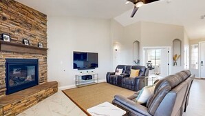Una sala de estar con chimenea de piedra, sofás de cuero, televisor de pantalla plana y ventilador de techo.