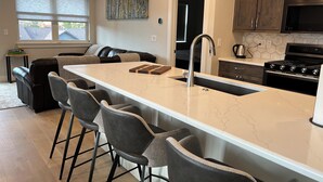 A modern kitchen with a large island, bar stools, a built-in oven, and a microwave.