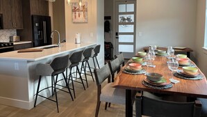 A modern kitchen with a central island, bar stools, and a dining table set for six with glassware and bowls.