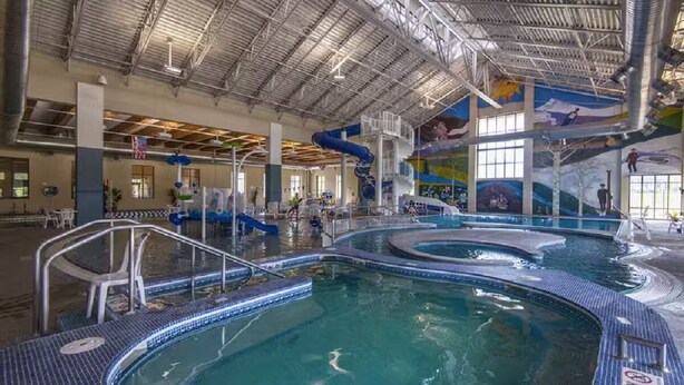 An indoor swimming pool with multiple lanes, a diving platform, and a mural on the ceiling.