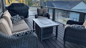 A covered outdoor seating area with wicker furniture and a table, overlooking a residential neighborhood and mountains.