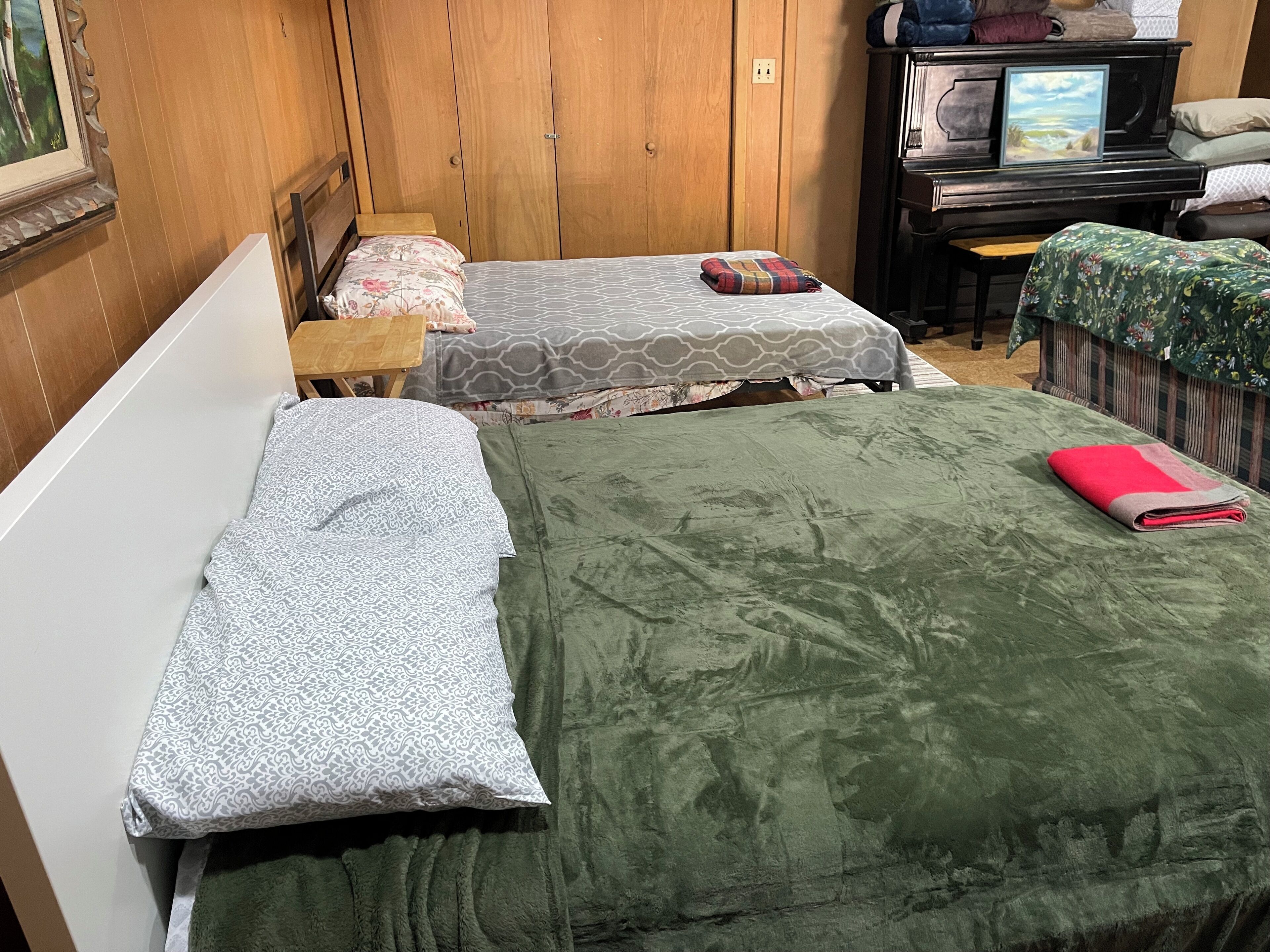 Une chambre avec deux lits, une armoire en bois, un téléviseur et un piano.