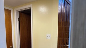 A hallway with a wooden door, a white wall with a light switch, and a carpeted staircase. - Room with Two DB Beds, Bathroom, Fridge, MW, TV, Wifi - 1 guest 64, 2 guests 120 (Silver Spring)