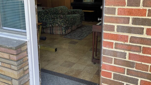 A room with a brick exterior, a wooden door, a bed with floral bedding, a television on a stand, and a piano. - Room with Two DB Beds, Bathroom, Fridge, MW, TV, Wifi - 1 guest 64, 2 guests 120 (Silver Spring)