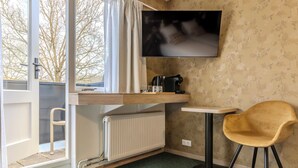 A compact hotel room with a kitchenette, a TV mounted on the wall, a small table, a chair, and a view through a window. - Hotel de Zon anno 1870 (Oosterwolde)