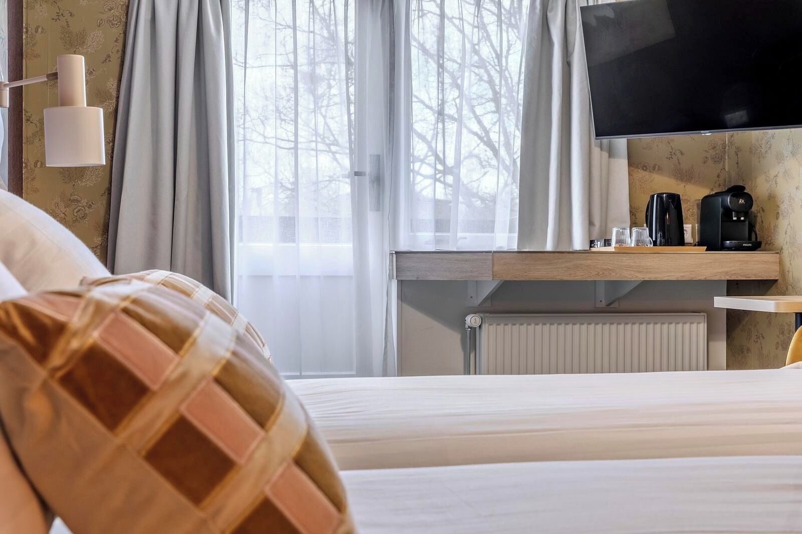 A hotel room with a bed, a TV, a coffee maker, and a window with curtains.