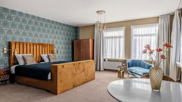 Un dormitorio con cama, cabecero de madera, sofá azul, mesa redonda y un jarrón con flores.