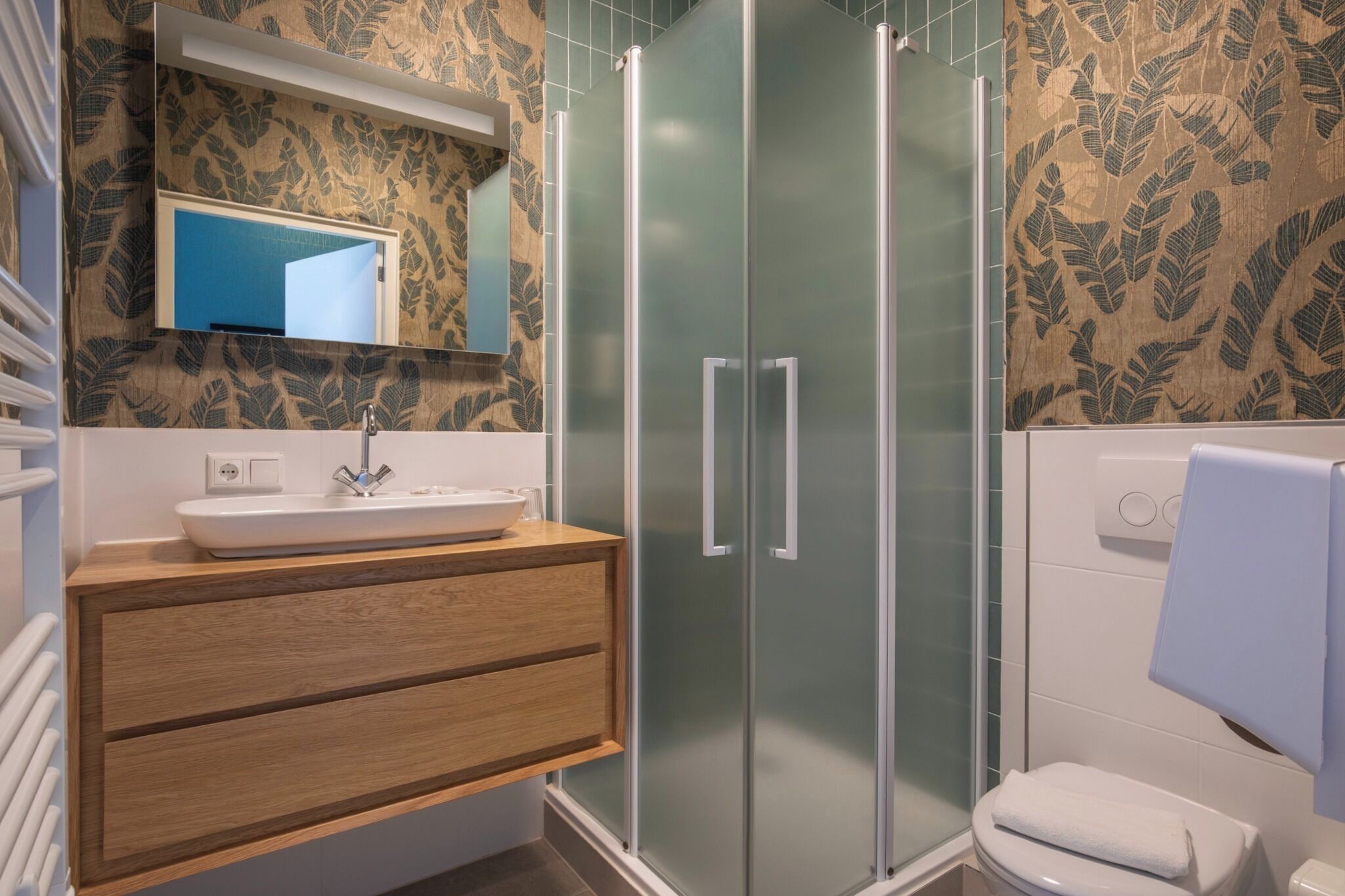 Un baño con tocador de madera, lavamanos, espejo, cabina de ducha de vidrio y toallero.