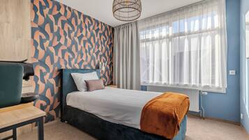 Una habitación de hotel moderna con una cama grande, un escritorio, una silla y una ventana con cortinas translúcidas.