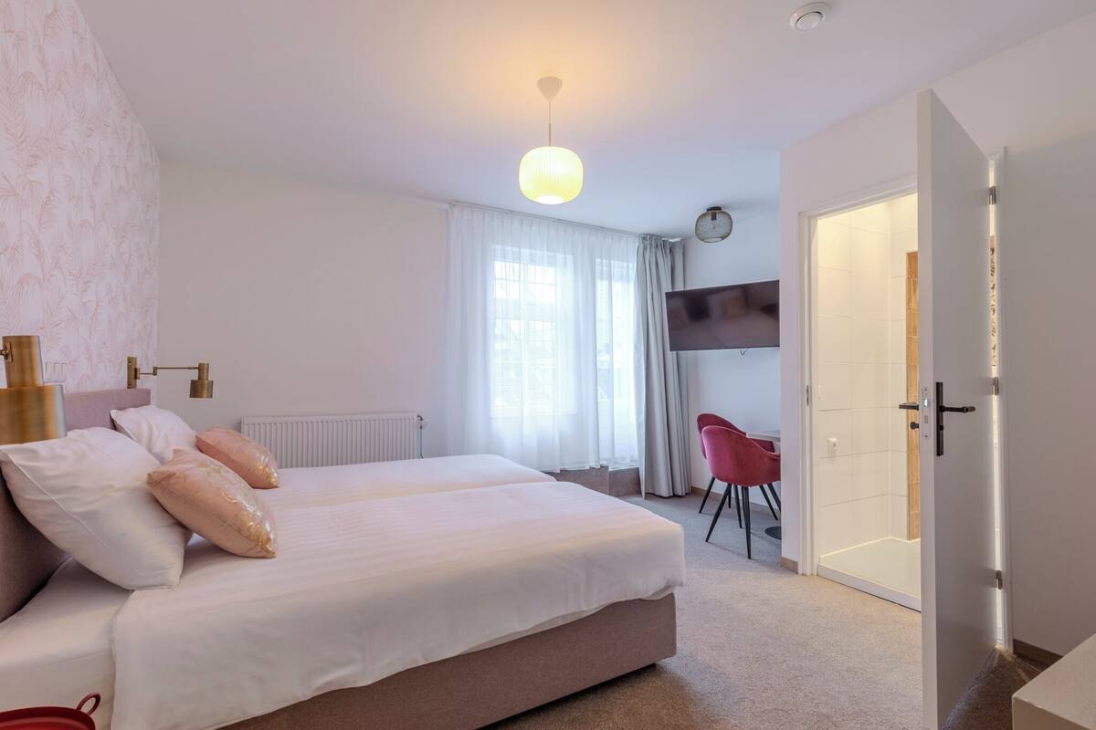 Une chambre moderne avec un grand lit, un téléviseur fixé au mur et une porte donnant accès à une salle de bain.