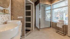 A modern bathroom with a large white sink, a glass shower enclosure, and a window with a view of the outside. - Hotel de Zon anno 1870 (Oosterwolde)
