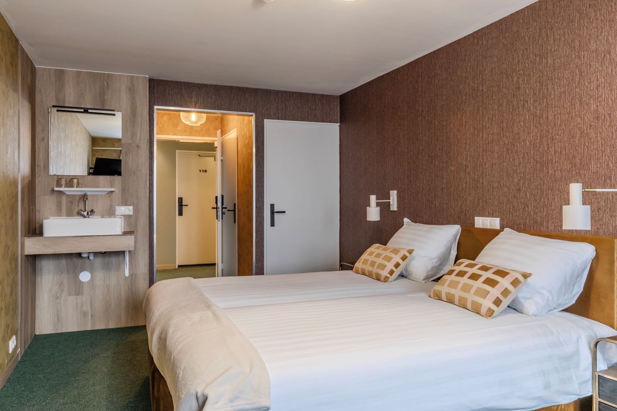 Een hotelkamer met een groot bed, nachtkastje, spiegel en een badkamer met wastafel en handdoekhouder.