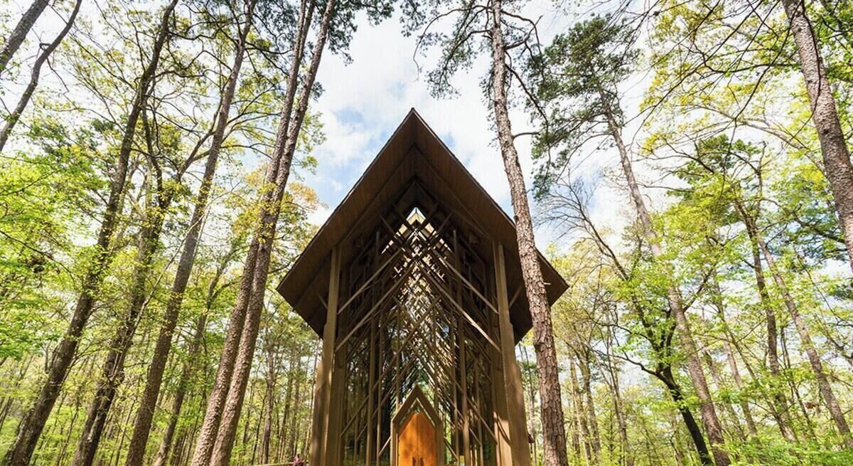 A wooden structure in a forest with a triangular roof and a central opening.