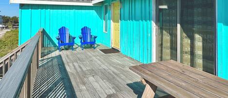 Een houten terras met twee blauwe Adirondack stoelen en een houten tafel.