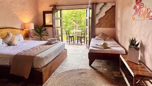 A hotel room with two beds, a balcony, a dining area, and a view of greenery. - Kikazaru Boutique Hotel (Quepos)