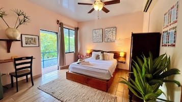 Une chambre à coucher comprenant un lit, des lampes de chevet, un ventilateur de plafond, un bureau, une chaise, une grande fenêtre et une plante en pot.