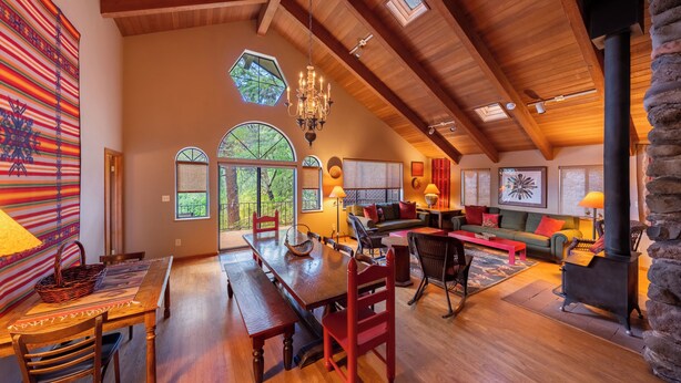 A spacious loft with a high ceiling, wooden beams, a dining area, a fireplace, and large windows. - Briar Patch Inn (Sedona)