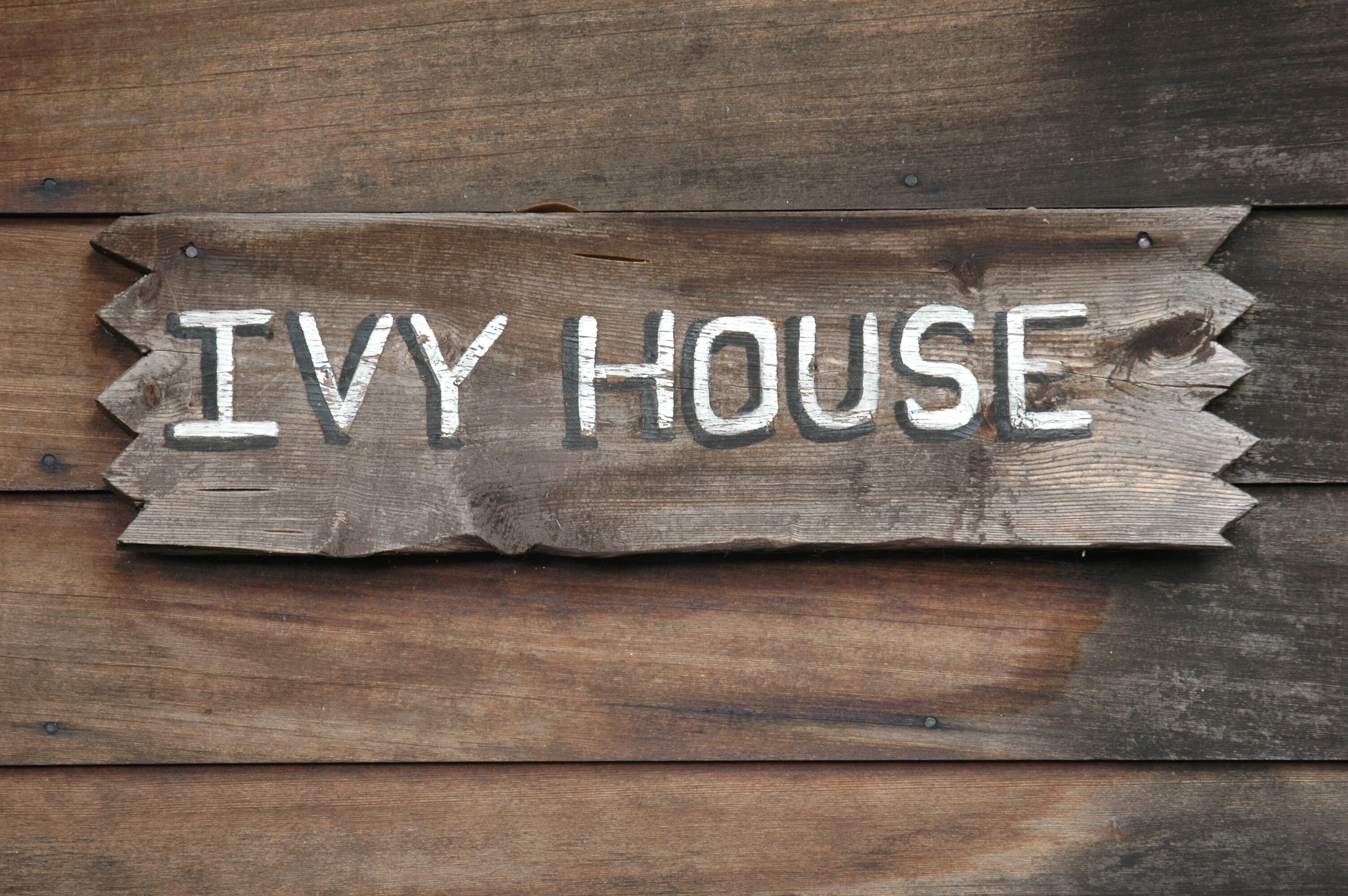 Een houten bord met de tekst 'Ivy House' op een houten achtergrond.