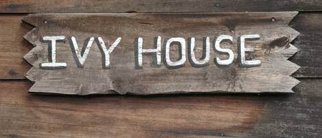 Een houten bord met de tekst 'Ivy House' op een houten achtergrond.