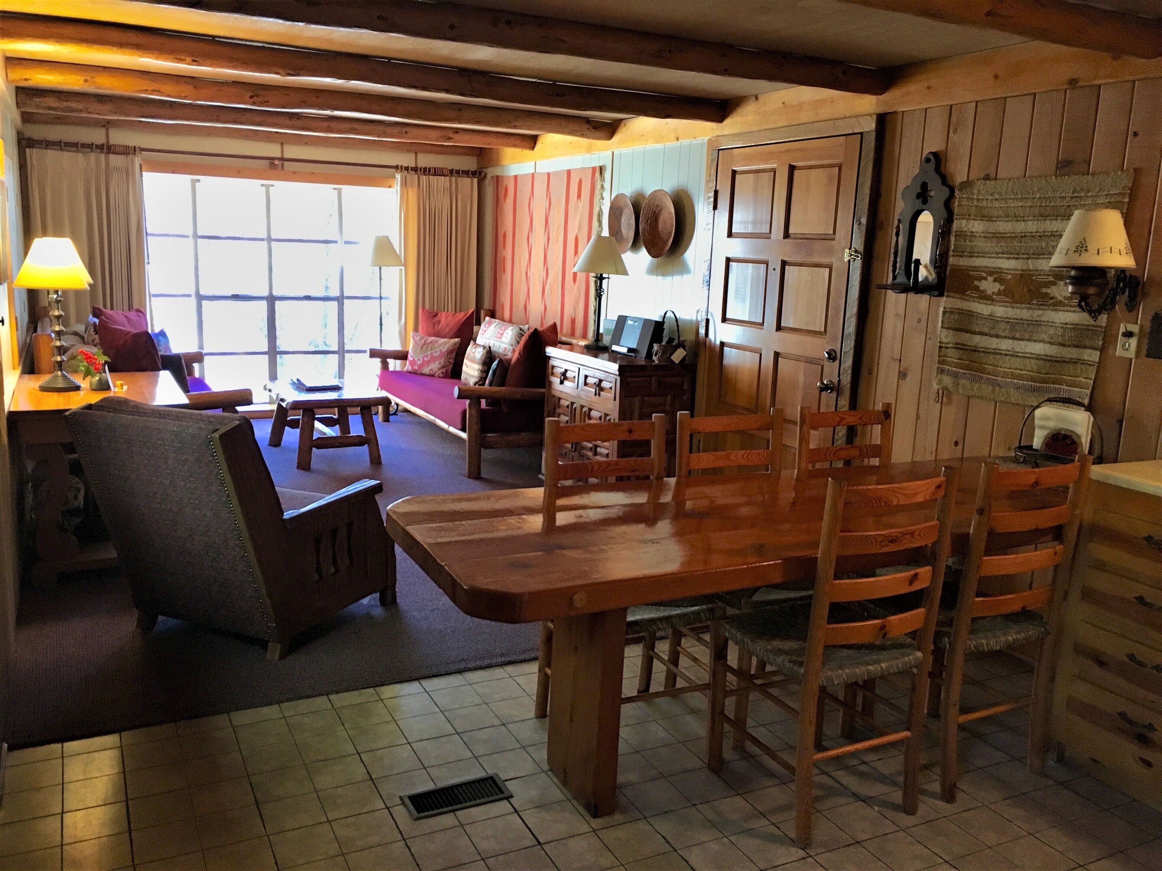 A cozy living room with a wooden dining table, chairs, a sofa, and a fireplace.