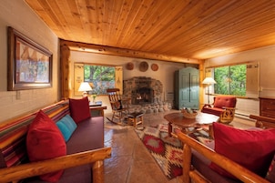 A cozy cabin interior with a stone fireplace, wooden furniture, and a stone floor.