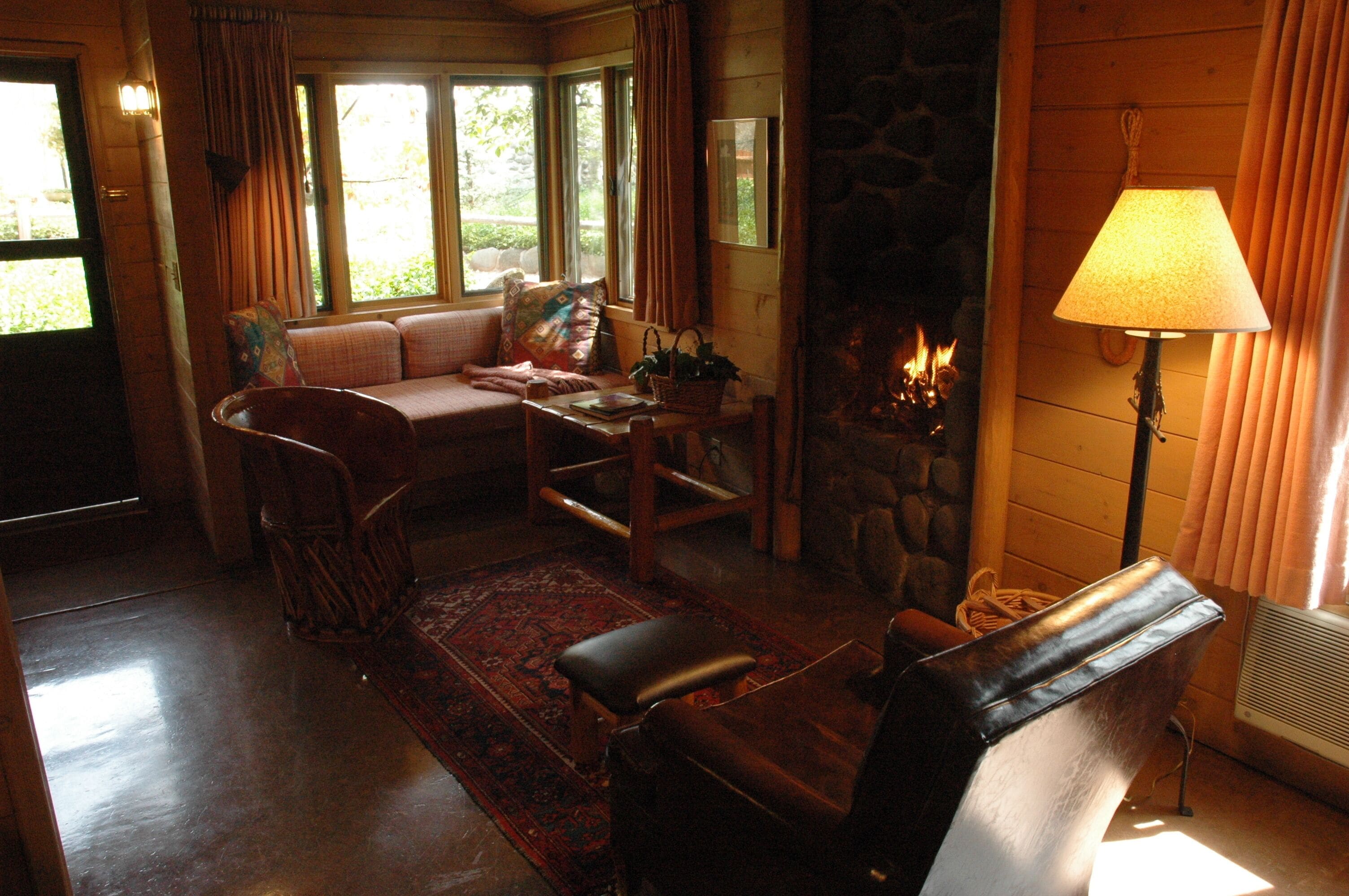 A cozy living room with a stone fireplace, a sofa, a dining table, and a lamp.