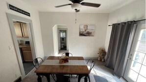 Un comedor con una mesa y sillas de madera, un ventilador de techo y vistas al exterior a través de un ventanal corredero.