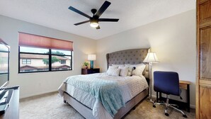 A bedroom with a bed, a desk, a chair, a ceiling fan, and a window with blinds.