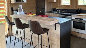 Een moderne keuken met houten kastjes, een centraal eiland met barstoelen, een inbouwoven en hanglampen.
