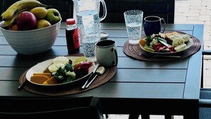 A dining table with a fruit bowl, plates of food, and drinks, overlooking a swimming pool.