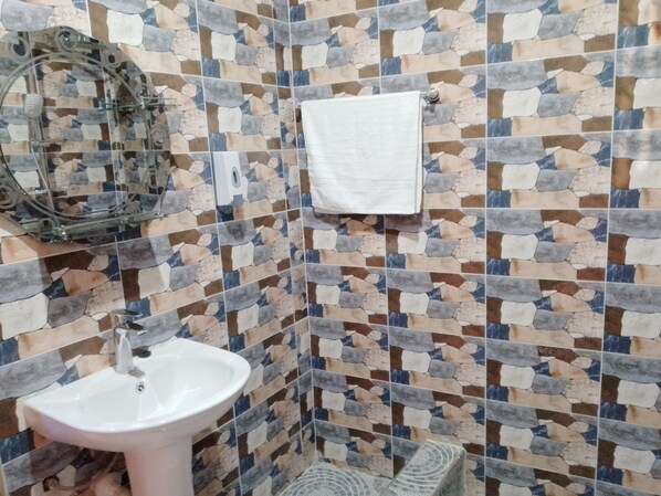 Un baño con pared de mosaicos, un lavamanos blanco y una toalla colgada en la pared.