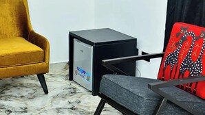 Ein Zimmer mit einem gelben Sessel, einem schwarzen Beistelltisch mit kleinem Kühlschrank und einem Stuhl mit roten und schwarzen Mustern.