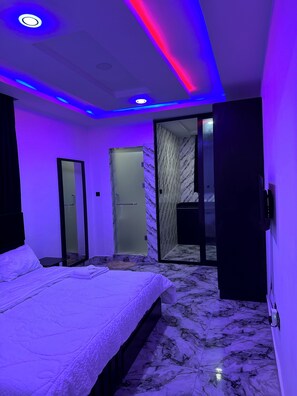 A modern bedroom with a bed, a walk-in closet, and a bathroom with a glass shower. - WIN4 LEISURE HOME AND APARTMENT LIMITED (Lagos)