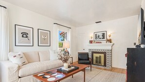 Un salon avec un canapé, une table basse, une cheminée et des tableaux encadrés accrochés au mur.