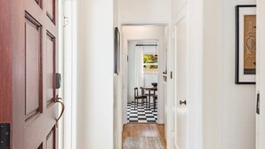 Un couloir avec une porte en bois, un sol à carreaux, un tapis et un tableau encadré accroché au mur.