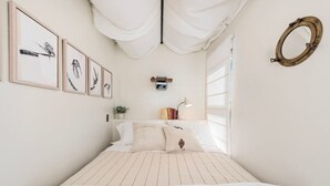 Une chambre à coucher avec un lit, une table de chevet avec des livres et une lampe, une caméra fixée au mur et des œuvres d’art encadrées.
