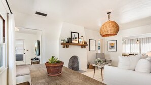 A modern living room with a wooden dining table, white sofa, and a hanging wicker light fixture.