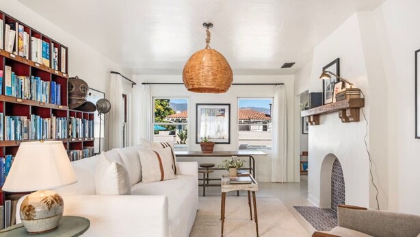 A living room with a white sofa, a bookshelf, a hanging wicker lamp, and a fireplace.