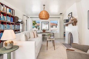 A living room with a white sofa, a bookshelf, a hanging wicker lamp, and a fireplace.