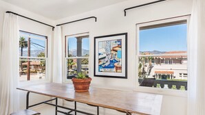 A dining area with a wooden table and benches, large windows with curtains, and a potted plant.