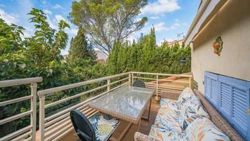 Een balkon met een rieten tafeltje en stoelen, een bank met bloemenkussens en een leuning.