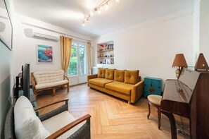 A living room with a sofa, a chair, a piano, and a bookshelf.