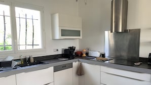 Cuina moderna amb armaris blancs, campana d'extracció en acer inoxidable, microones integrat i finestra amb vista a vegetació.